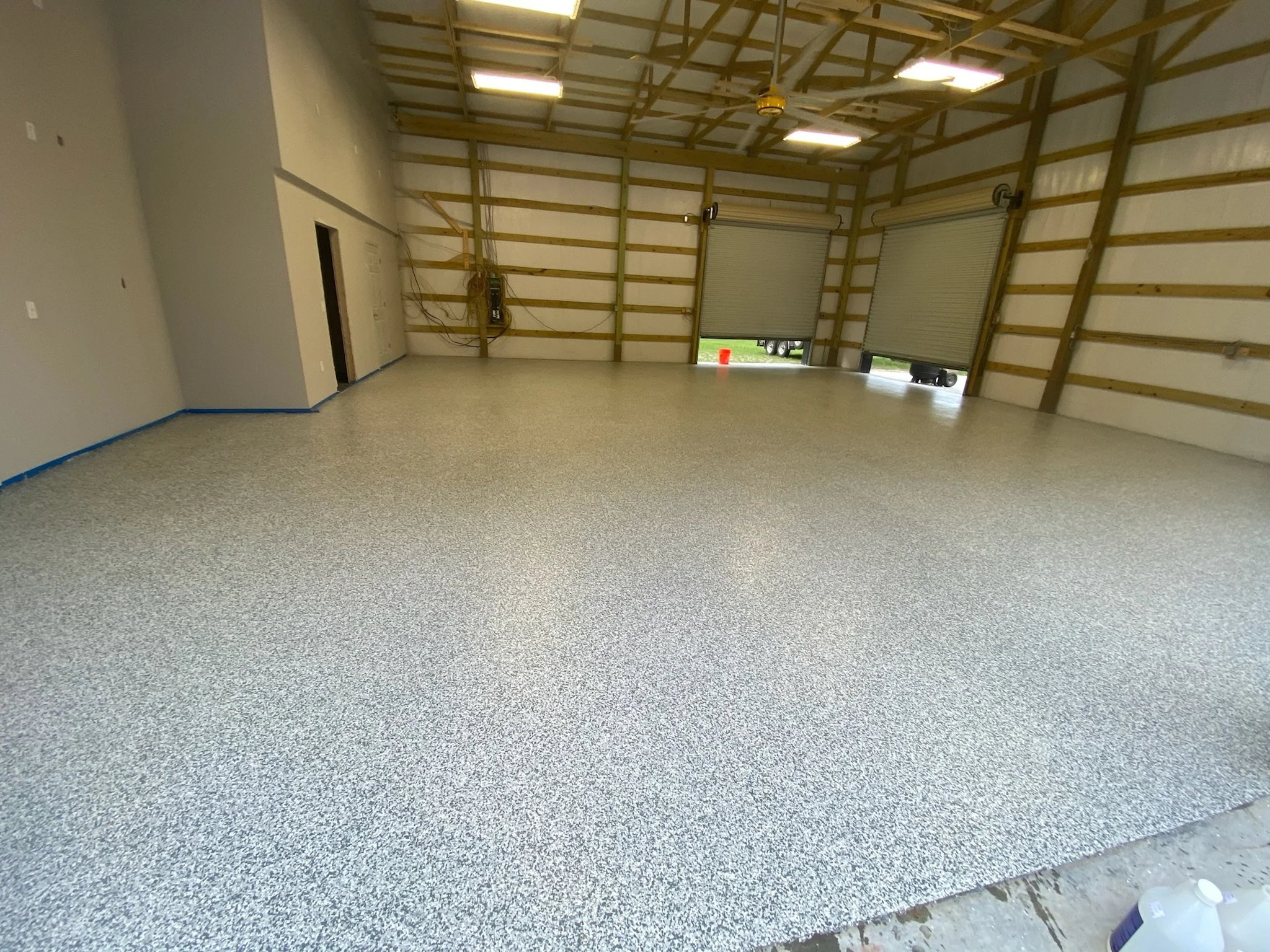 Empty industrial garage with new speckled epoxy flooring, unfinished walls, and two open garage doors.