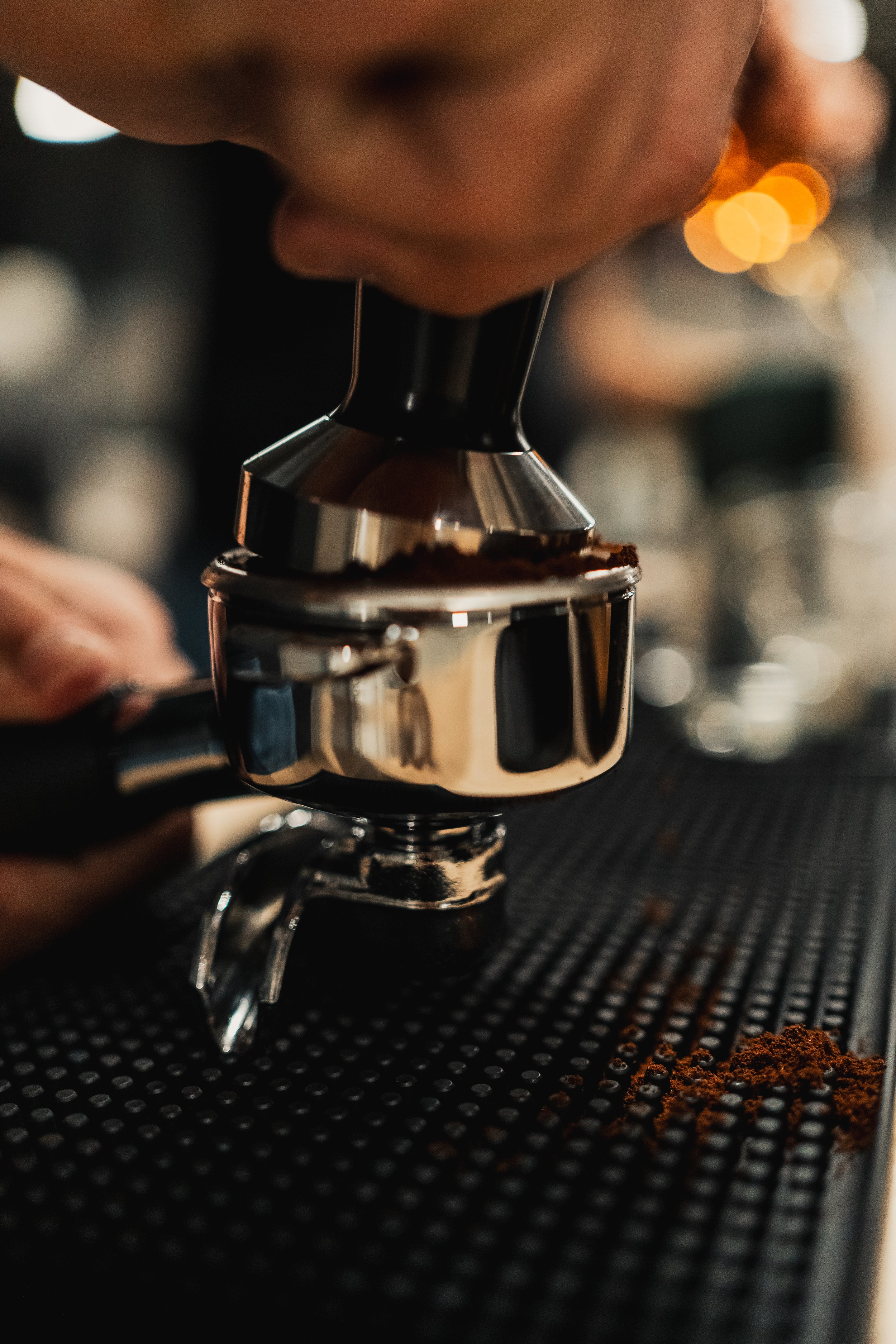 Close-up of a barista using a portafilter to tamp coffee grounds in an espresso machine in a coffee shop.