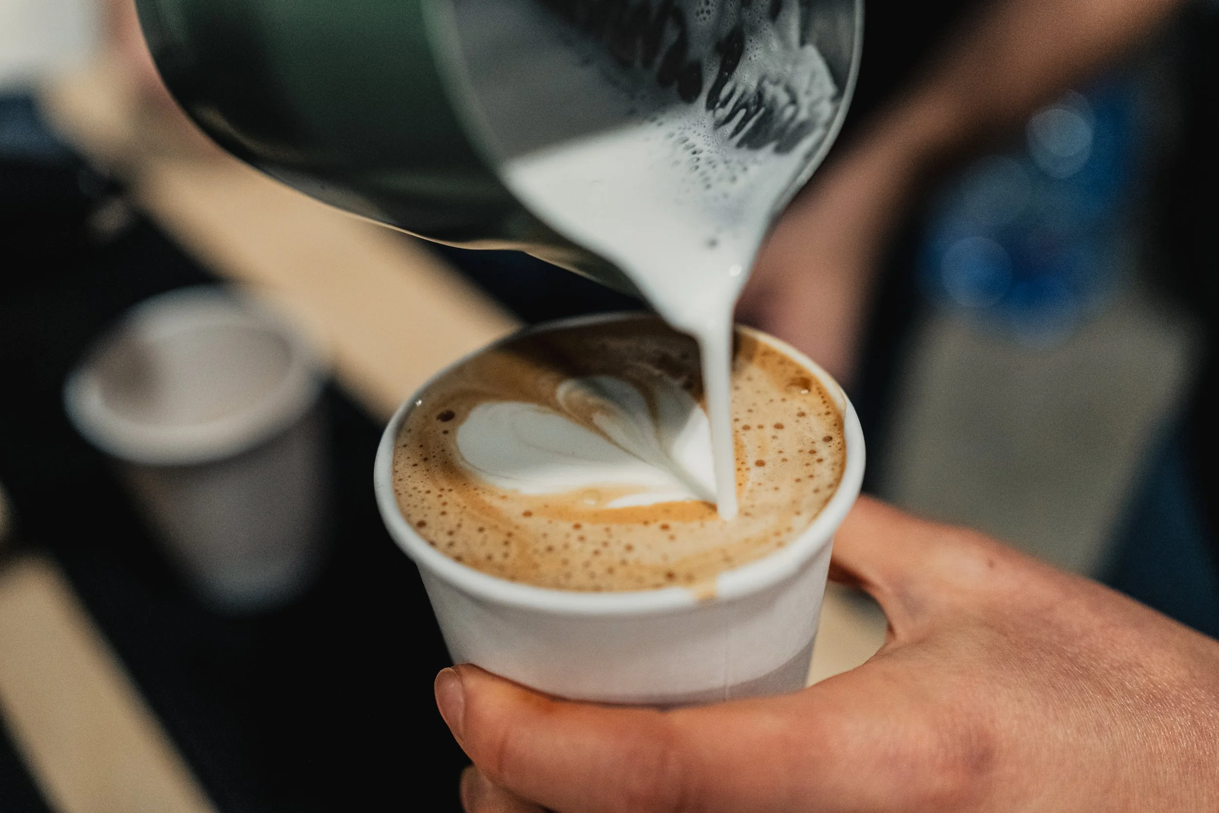 Barista pouring steamed milk into a cup of espresso, creating latte art.