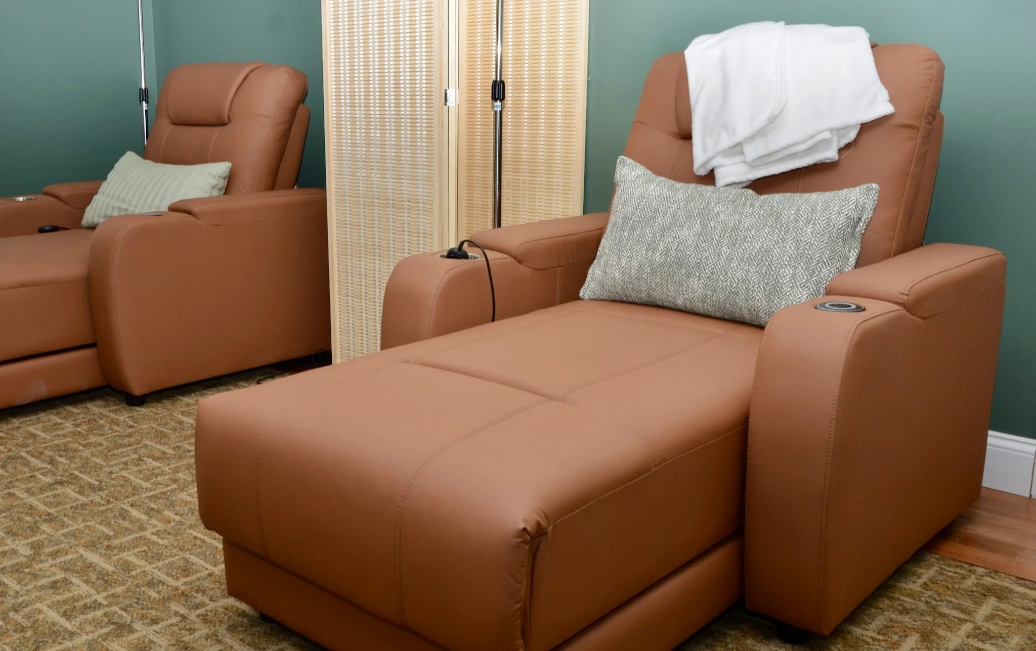 Two brown reclining chairs with pillows, separated by a folding privacy screen, in a room with green walls and beige patterned carpet.