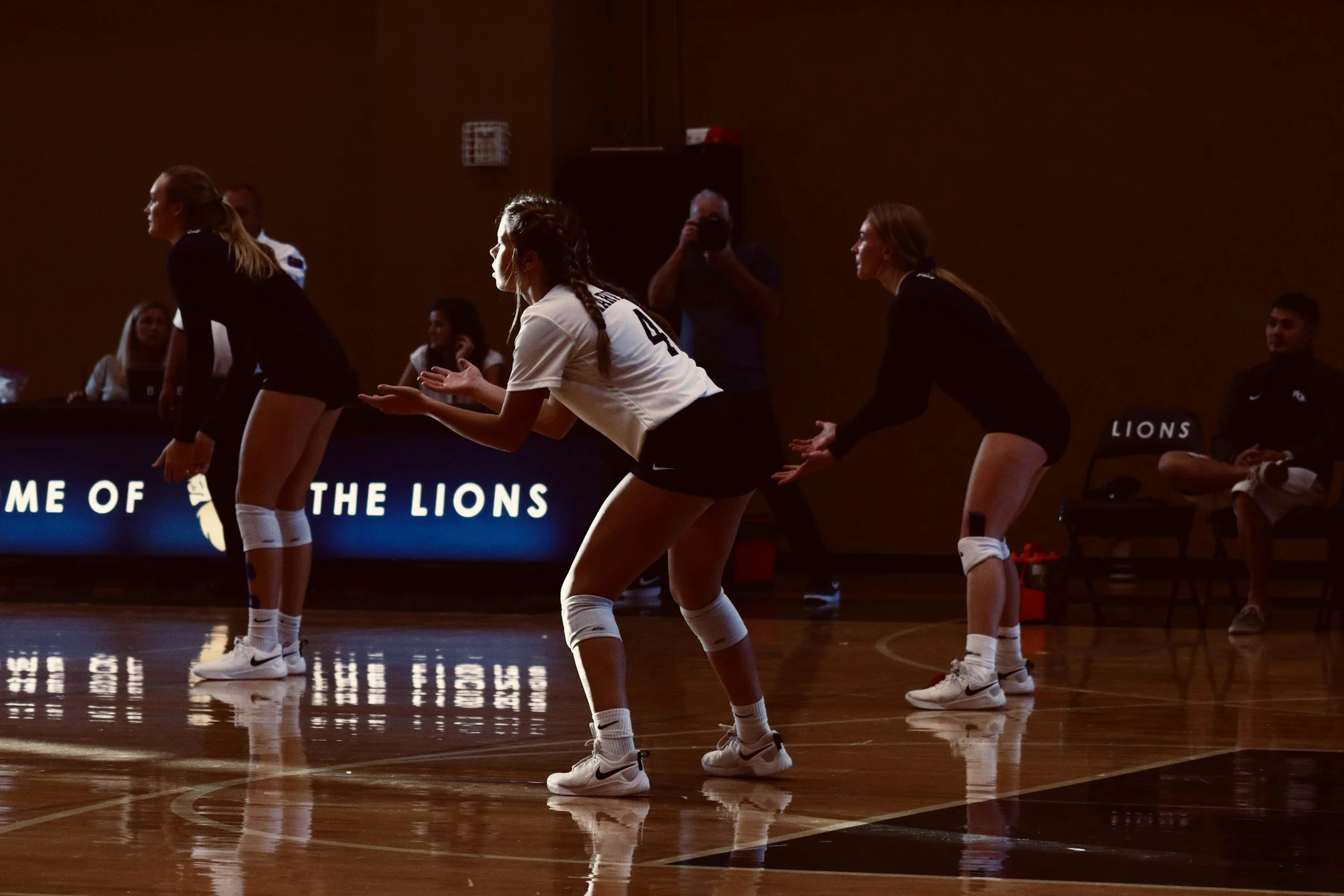 Women volleyball players in black and white uniforms performing a dance or warm-up routines on a gymnasium floor during a game or practice.