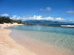 Empty sandy beach with clear blue water and a partly cloudy sky