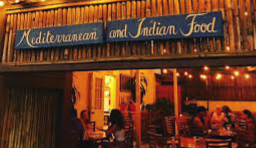 Sign reading 'Mediterranean and Indian Food' outside a restaurant with warm lighting and outdoor seating.