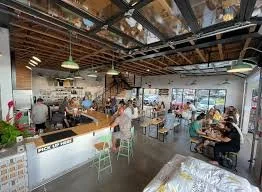 Interior of a busy cafe with customers, seating, and an industrial-style ceiling.