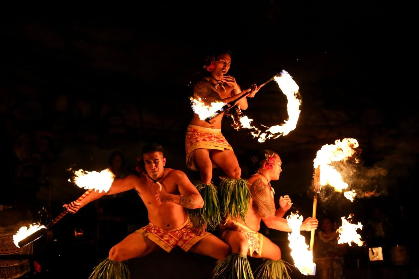 Three Polynesian fire dancers performing at night with flames, showing traditional costumes and dance moves.