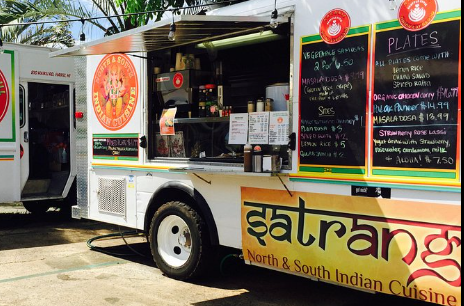 Food truck with menu sign, featuring Indian cuisine and vegetarian options, parked outdoors.
