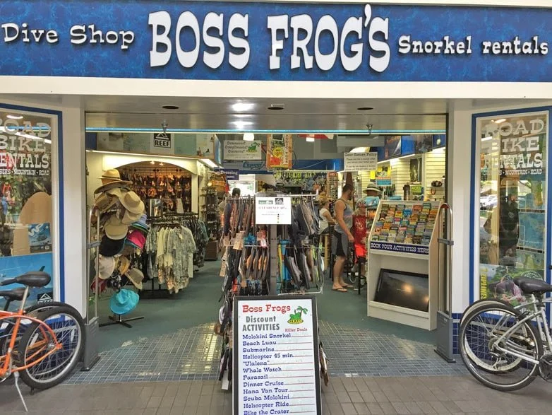 The entrance to Boss Frog's, a dive shop and snorkel rentals store, with clothing, hats, and equipment visible inside, and bicycles parked outside.