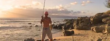 Person standing on a sandy beach holding a fishing rod during sunset or sunrise.