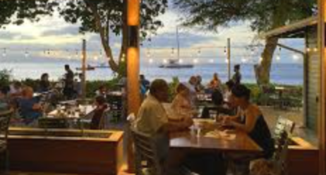 People dining at an outdoor restaurant with a view of the water and boats