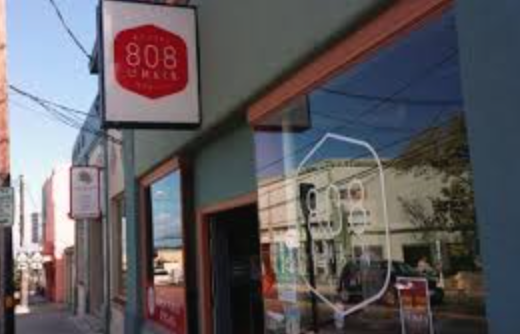 Close-up of a store window with a white August Burns Red band logo outline and an outdoor sidewalk scene reflecting in the glass.