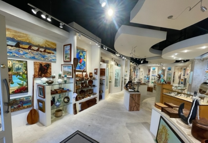 Interior of an art gallery displaying paintings and crafts on white walls and shelves, with a curved ceiling and bright lighting.