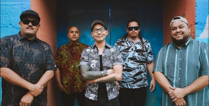 Five men standing against colorful painted walls, wearing casual shirts, sunglasses, and caps.
