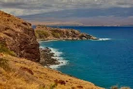 Coastal landscape with cliffs and blue ocean under cloudy sky.