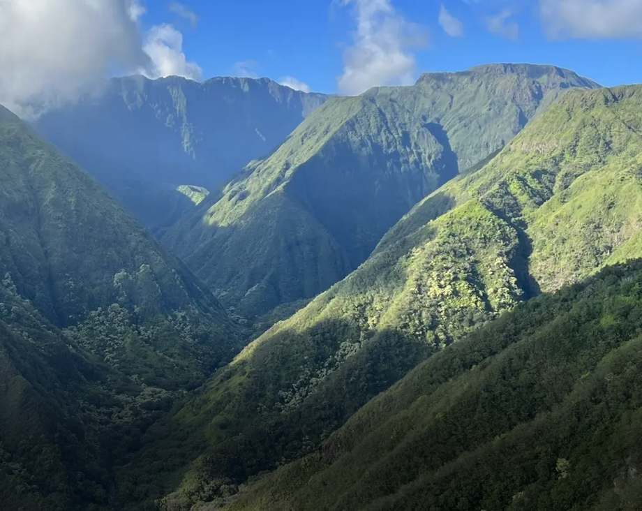 Lush green mountains with steep slopes under a partly cloudy blue sky.