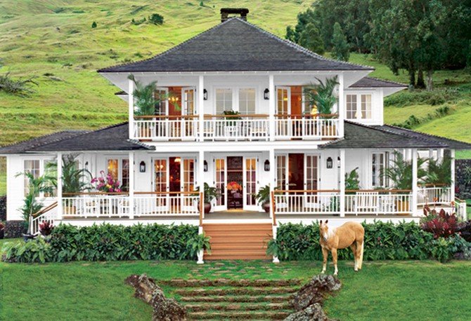 A large two-story white house with a wraparound porch, surrounded by greenery and trees with a grassy lawn in front. There is a horse grazing near the porch and stone steps leading up to the house.