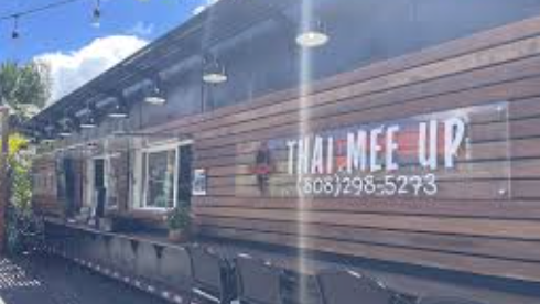 Sign on a train that reads "Thai Mee Up" with a phone number, next to windows and a wooden exterior.