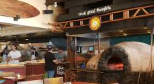 Interior of a restaurant with a wood-fired oven and staff preparing food at a counter.