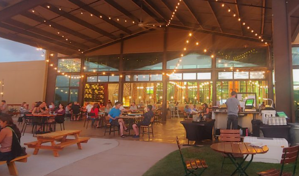 People dining inside a restaurant with large glass windows, string lights hanging from the ceiling, and outdoor seating visible.