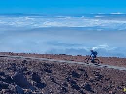 A person riding a bicycle on a dirt path in a desert landscape with cloudy sky.