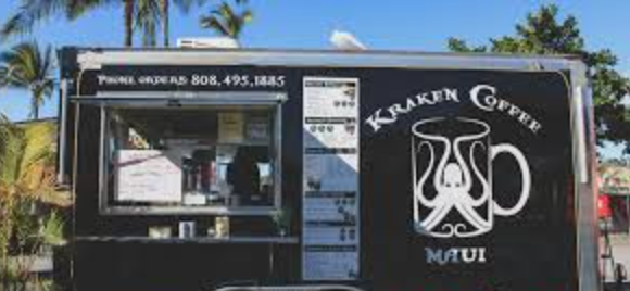 Food truck with black exterior and Kraken Coffee Maui logo, menu display, palm trees and blue sky in background.