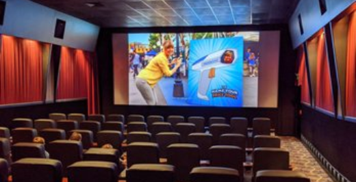 A woman taking a photo of a giant cartoon thumbs-up sign in a movie theater or auditorium.