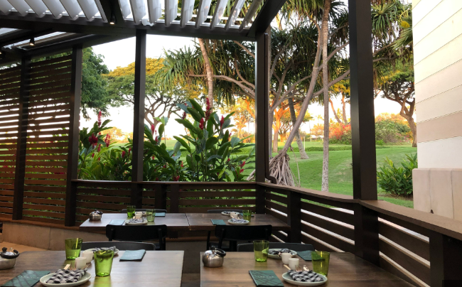 Outdoor deck with a dining table set for a meal, surrounded by lush greenery and trees, with a view of a park or garden area.