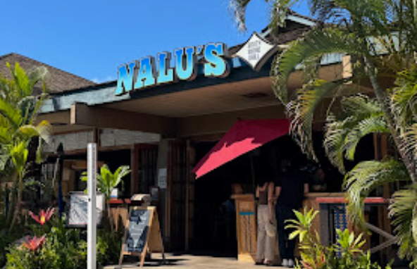 Exterior of Nalu's restaurant with tropical plants and people waiting outside under a pink umbrella.