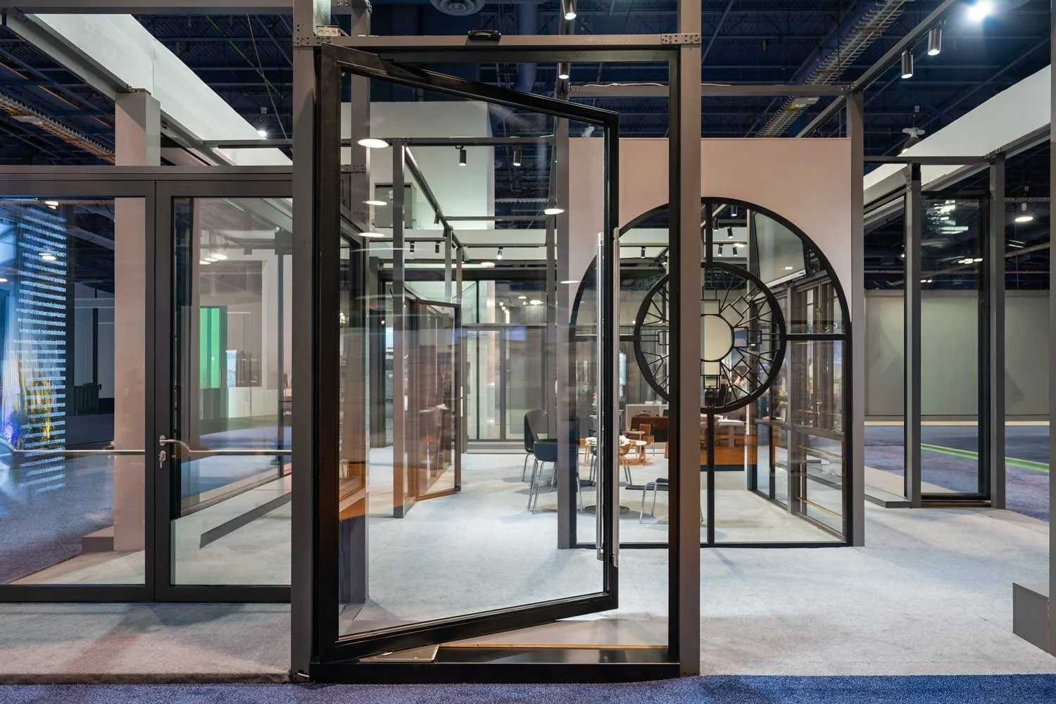Modern office space with glass walls, open door, and minimalist furniture, including a large circular decorative piece on the wall.