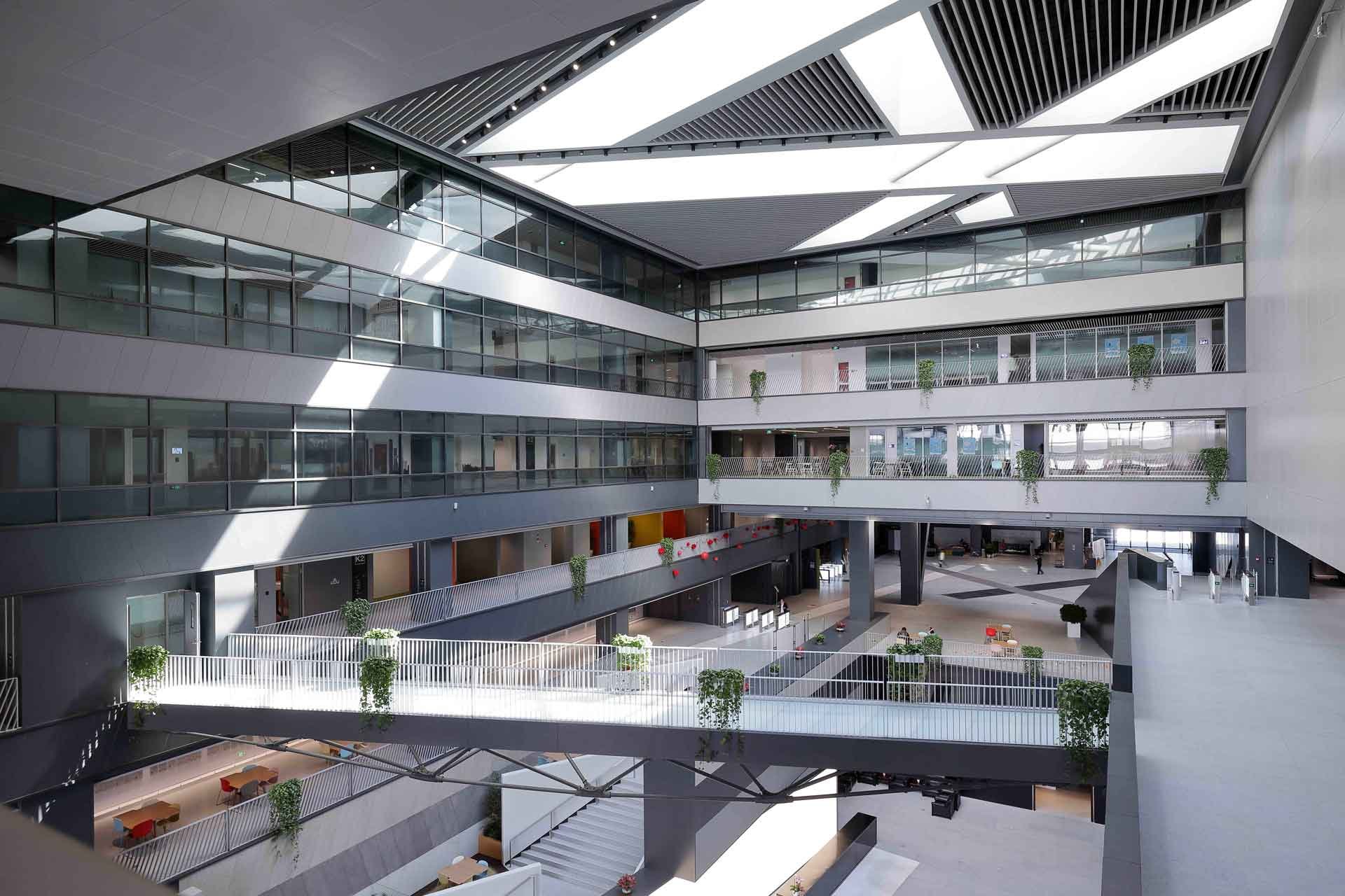 Interior view of a modern multi-story office building with curtain walls, open common areas, and potted plants on balconies.