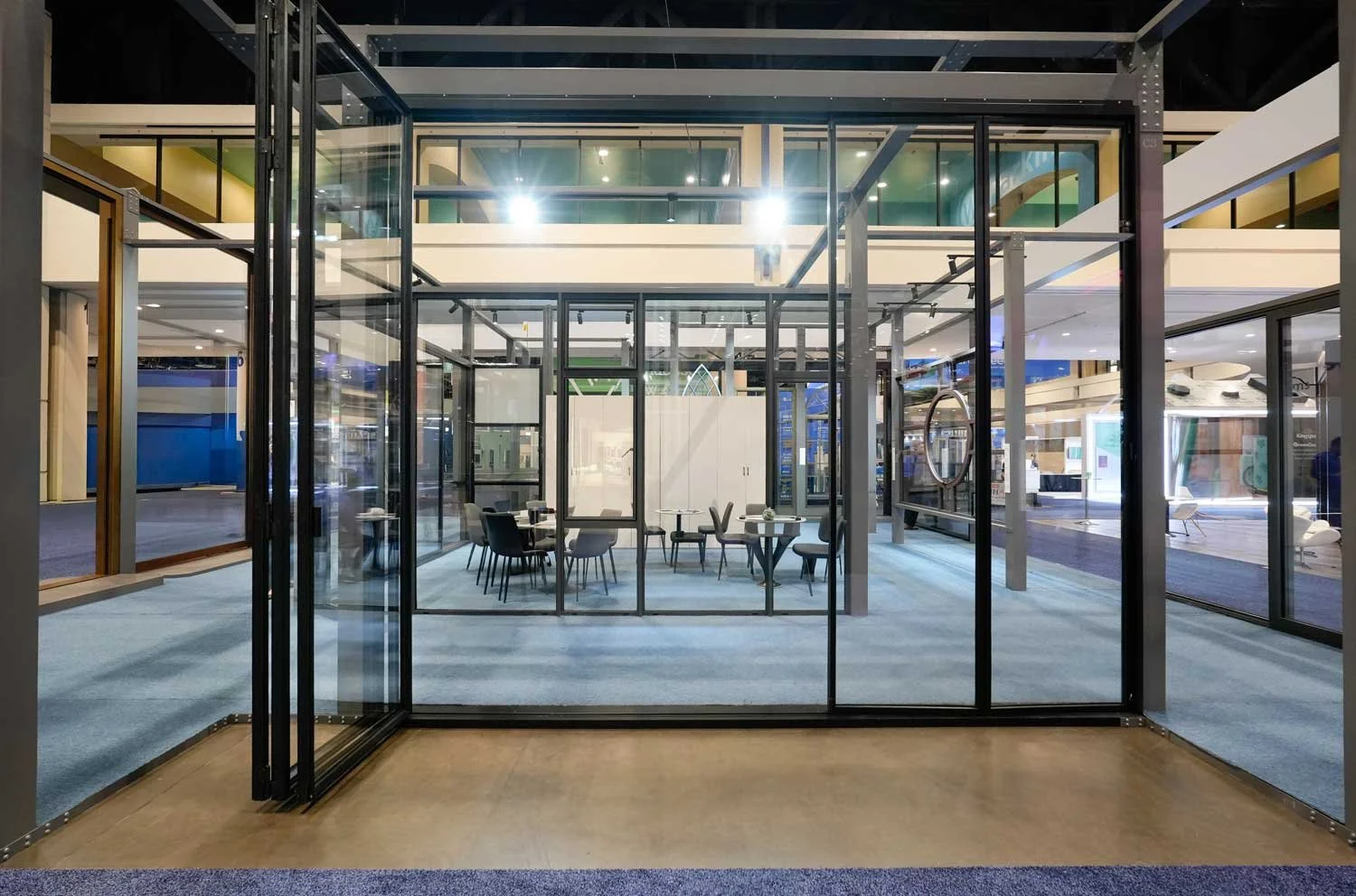 Modern glass-walled meeting space with chairs and tables inside a shopping mall or office building.