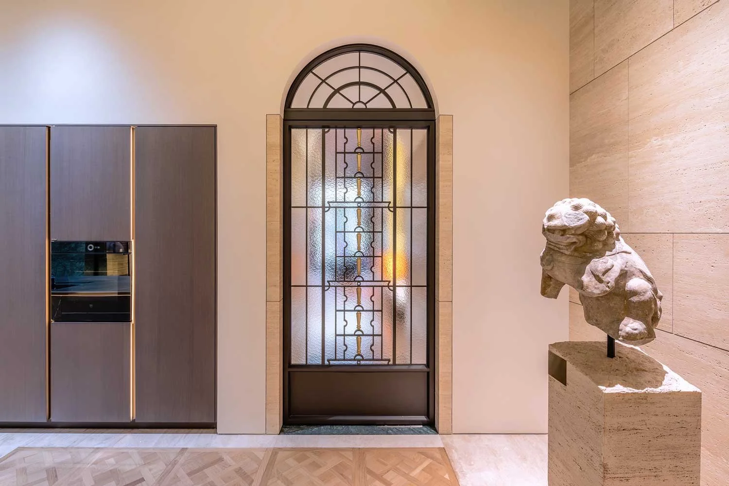 Interior view of a modern building with a decorative glass door, a stone sculpture of a lion, and built-in kitchen cabinetry.
