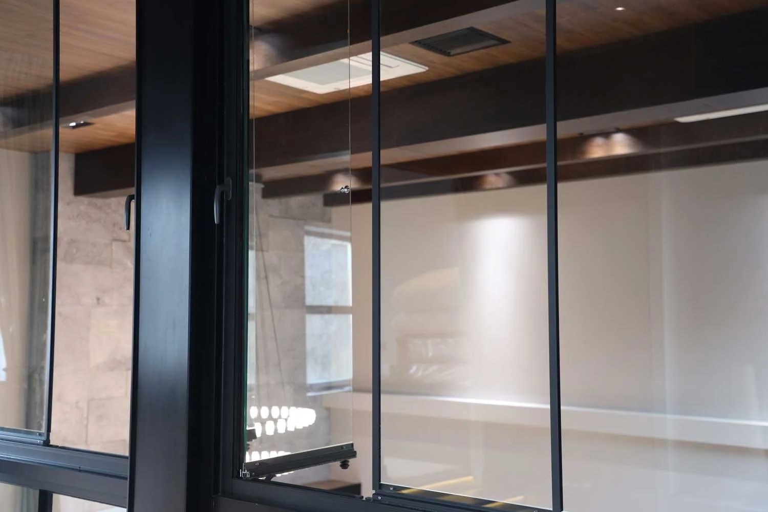 A close-up view of a large glass window with black metal framing, showing reflections of the interior and exterior surroundings.