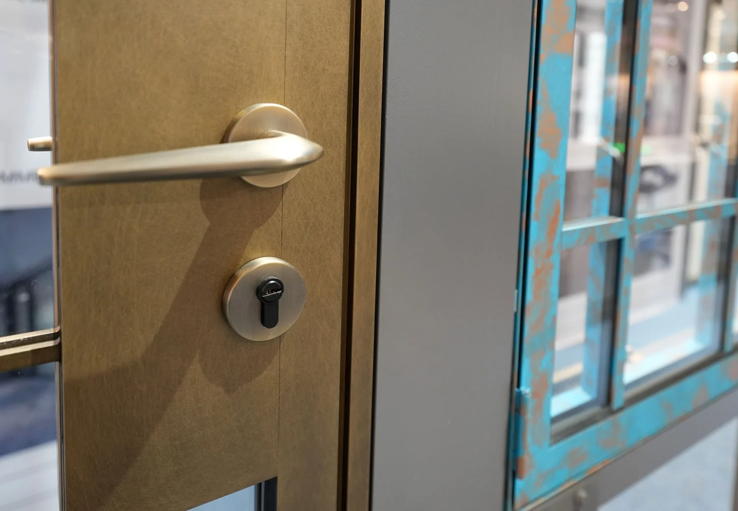 Close-up of a metallic door handle and lock on a beige door, with a building visible through large window panes to the right.