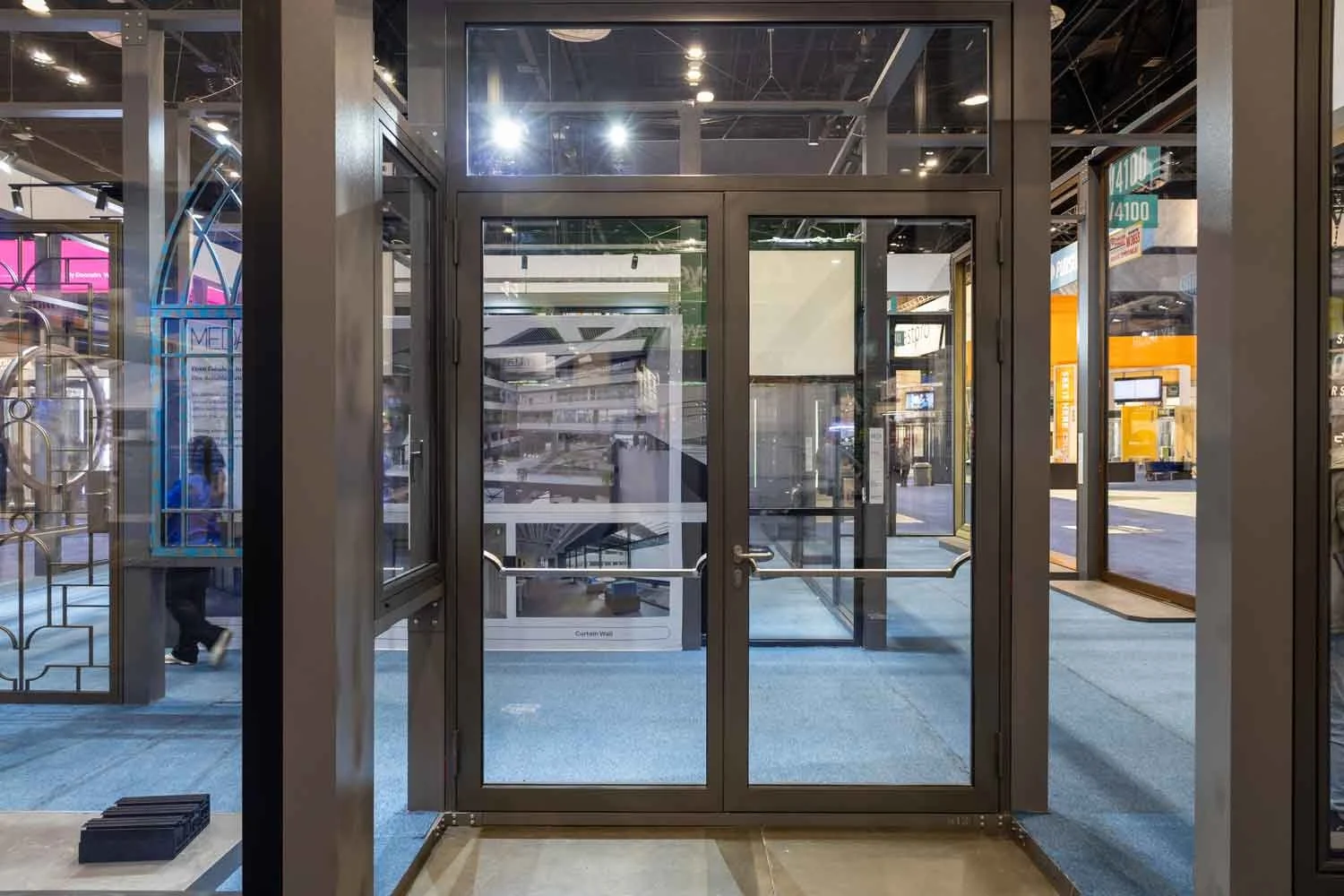 View of steel double door and window frame in a commercial space with a street scene outside, including signs and people walking.