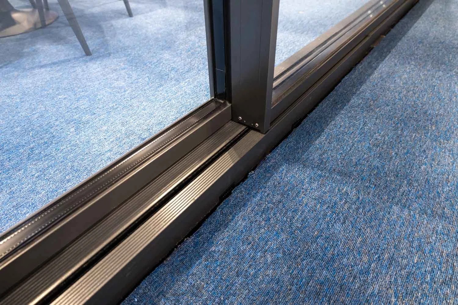 Close-up of a glass sliding door track with a blue carpeted floor.