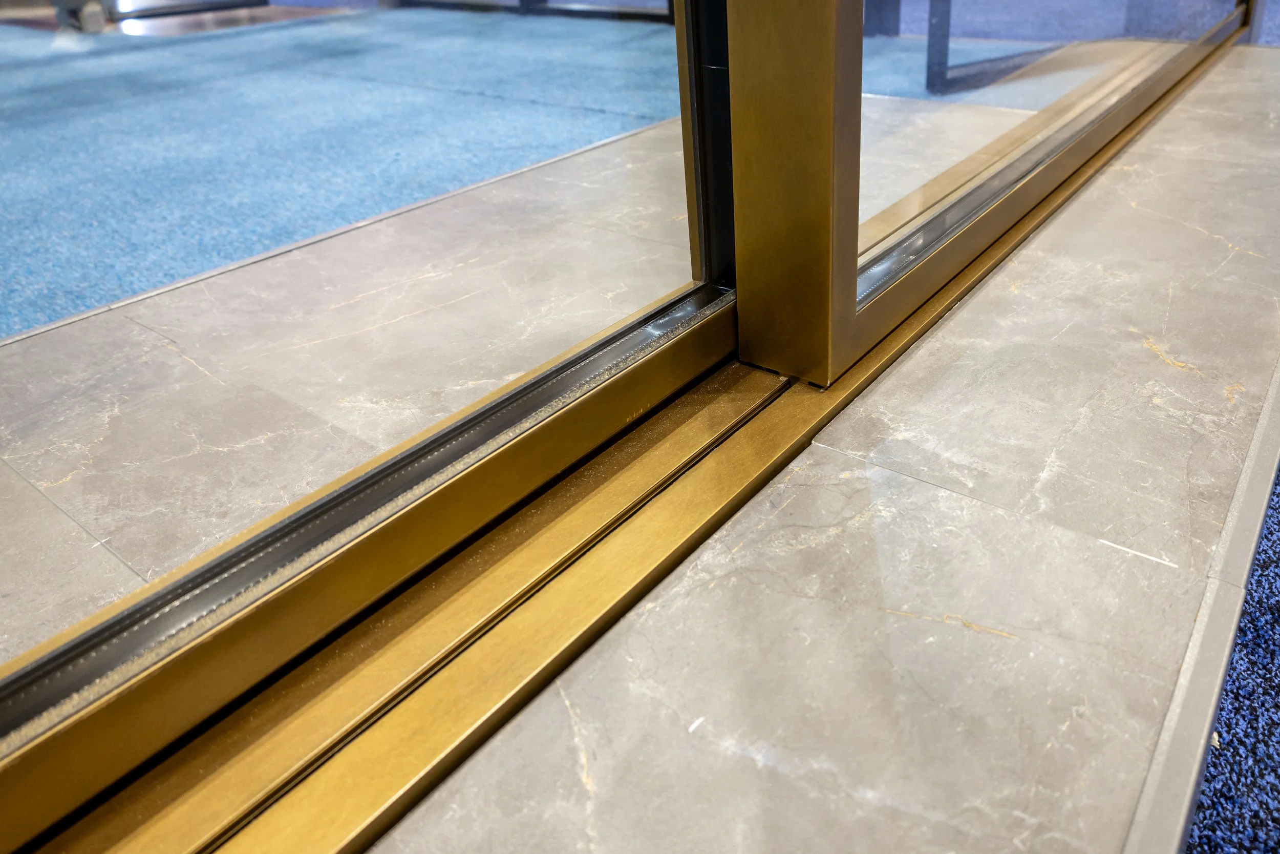 Close-up of a glass door with gold-colored metal frame and sliding track on a marble floor.
