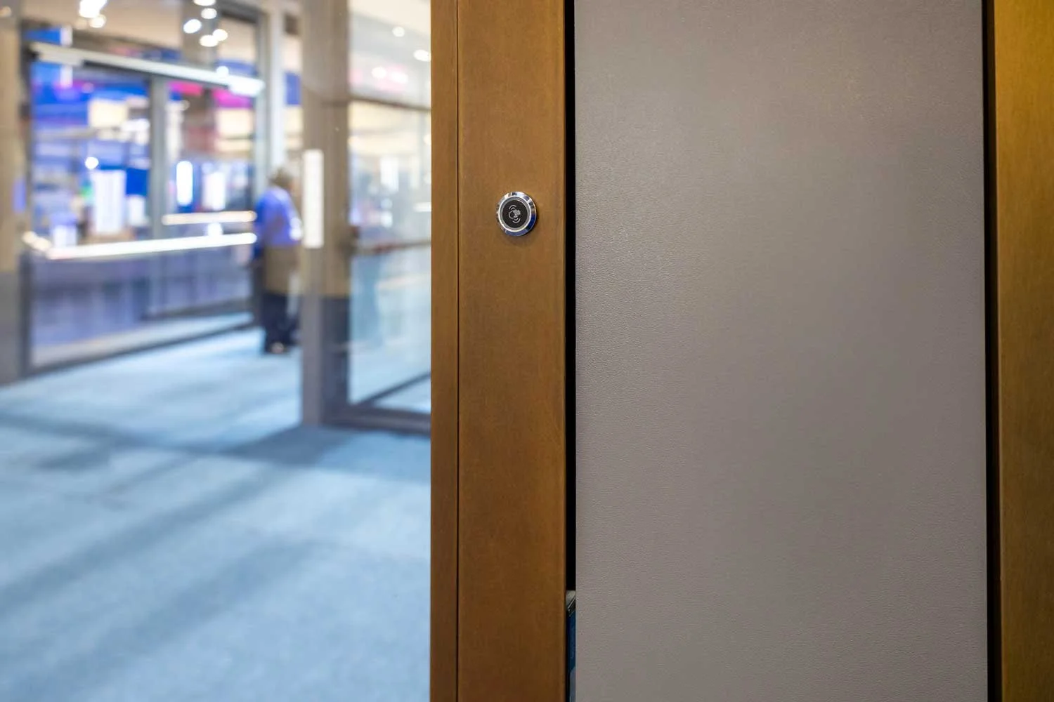 Close-up of a door latch with a keypad sensor in a trade show, with people and glass doors in the background.