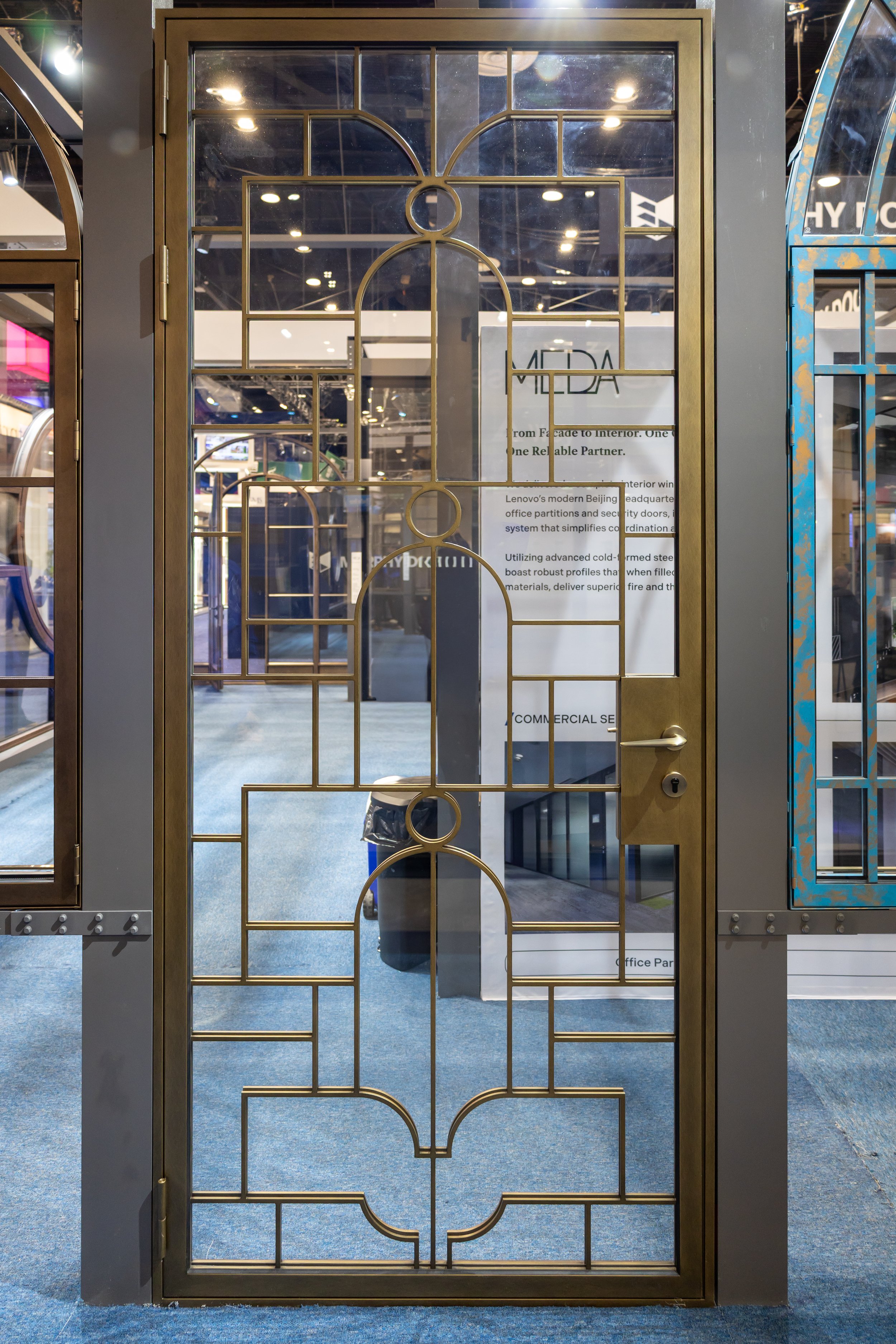 Decorative metal grid door with geometric patterns, seen in a showroom, with other metal framed doors visible on either side.