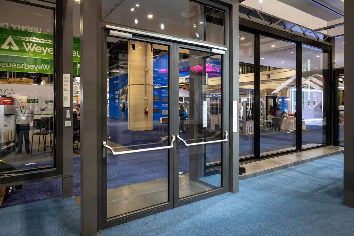 Entrance with steel-framed double doors leading into a trade show or convention center with booths, displays, and people inside.