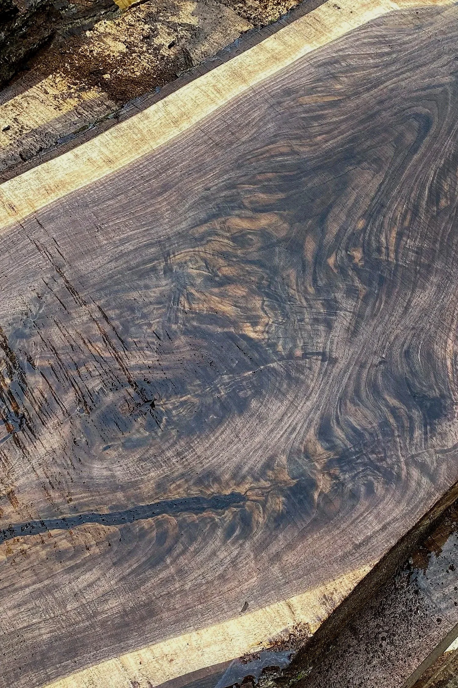 Close-up of a weathered, dark-stained wooden surface with visible grain and texture, surrounded by rough, bark-like wood edges.