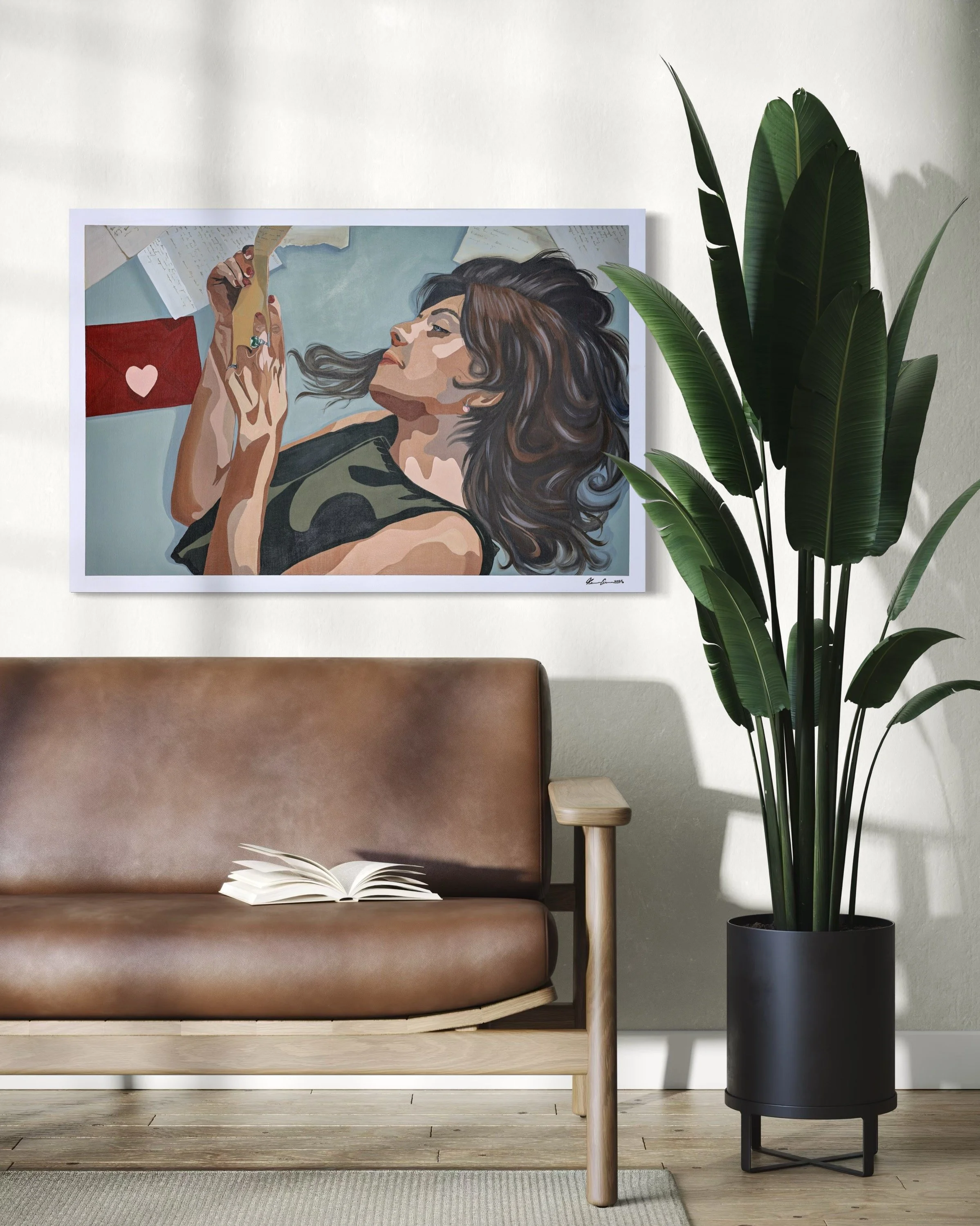 A living room with a brown leather couch, an open book on the couch, a large green potted plant, and framed artwork of a woman with long hair lying down, holding a card with a heart on it, on the wall.