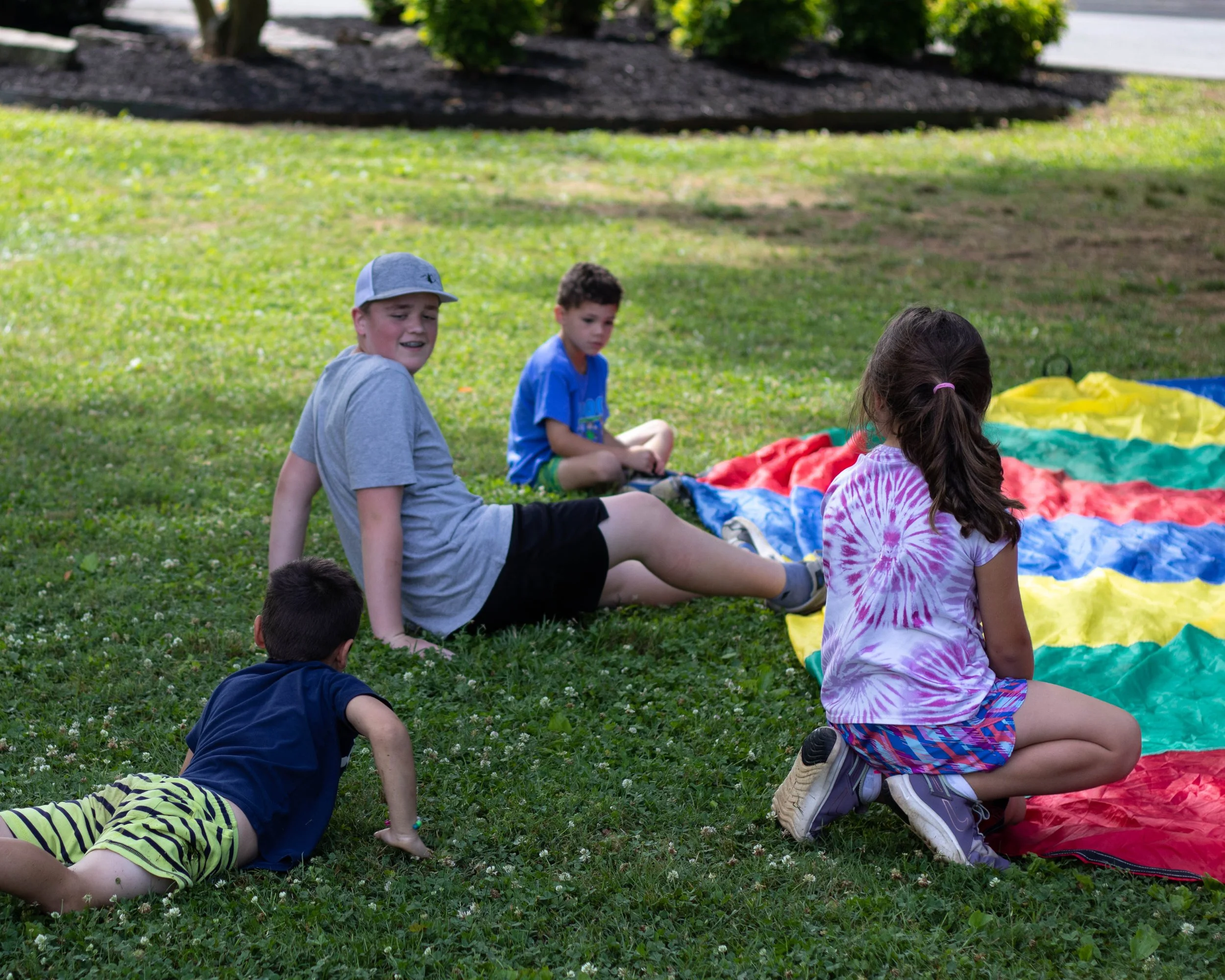 Four children playing on grass near a colorful parachute in a park.