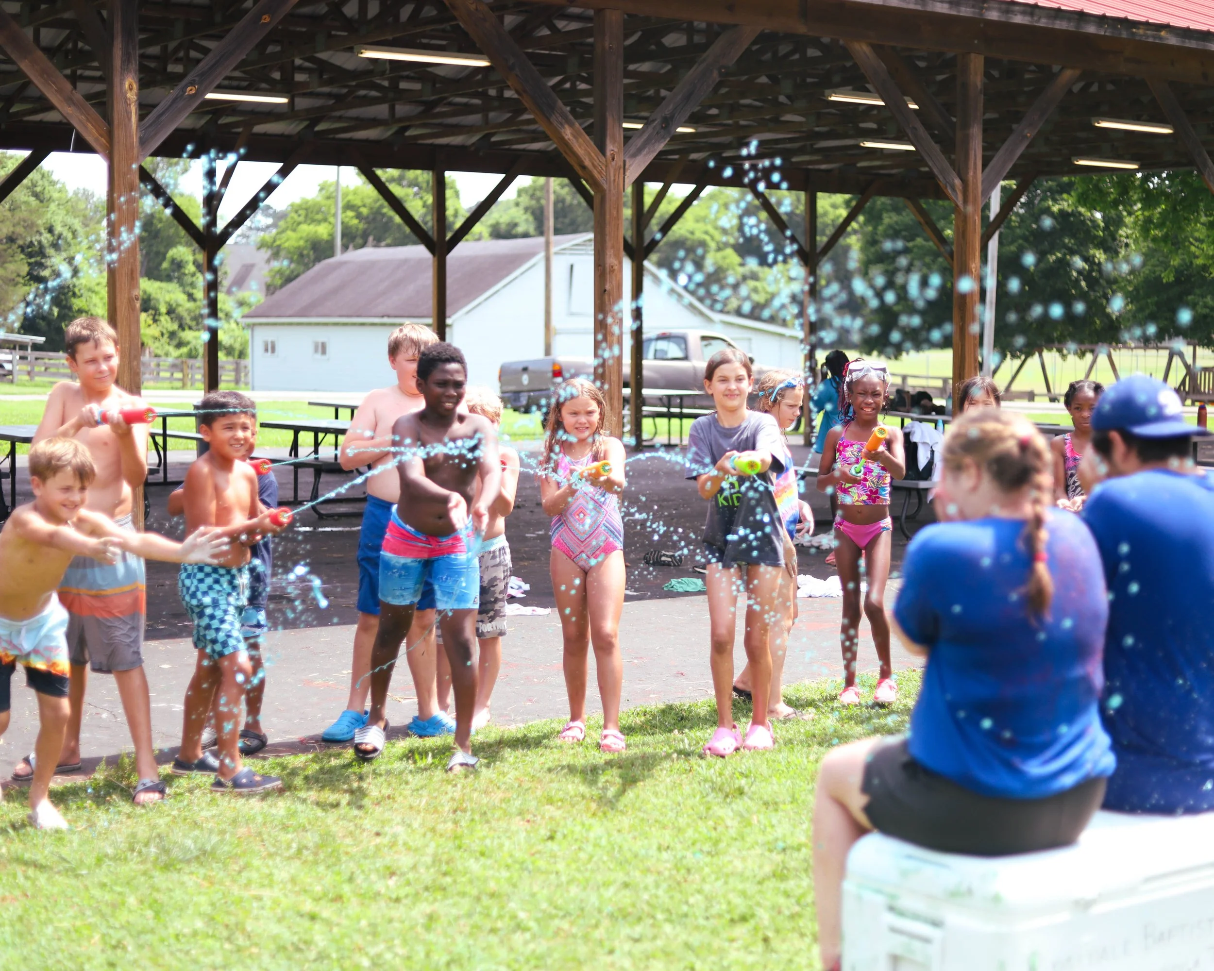 Children at a summer water fight, spraying water from water guns under a pavilion.