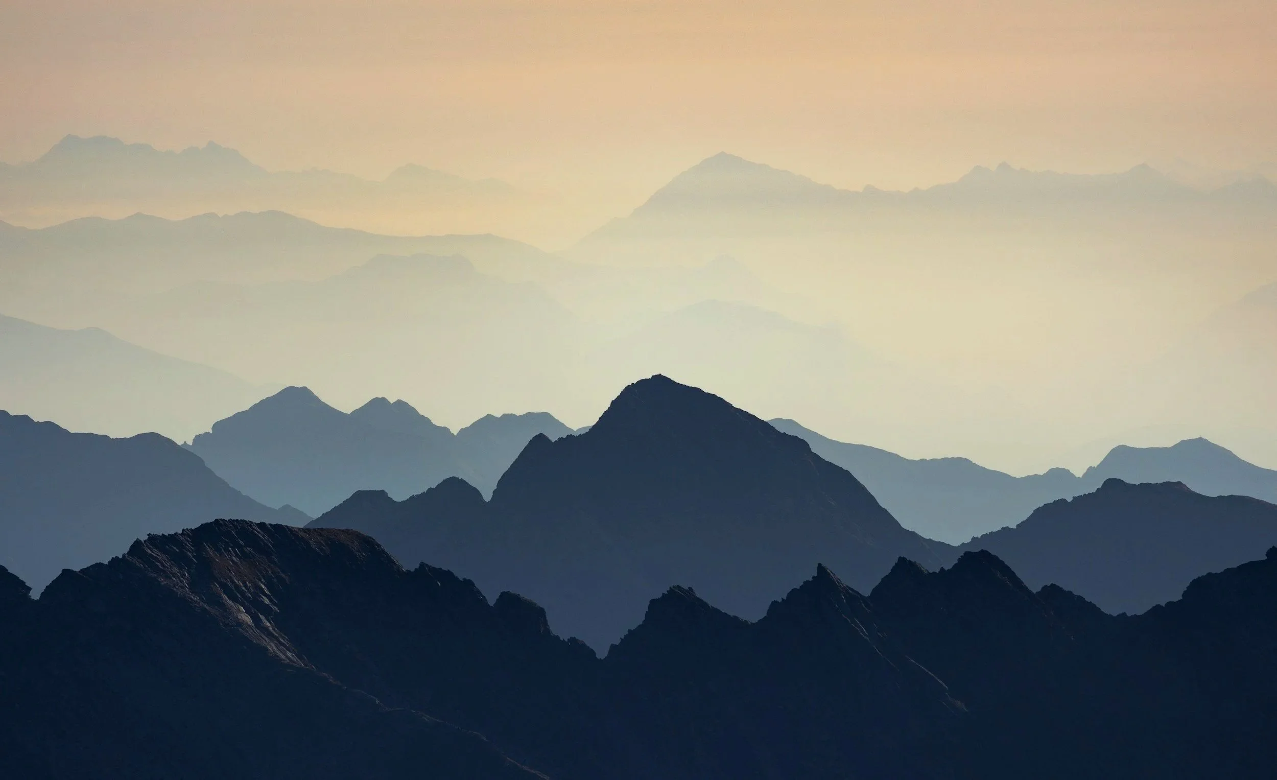 Silhouettes of mountain ranges fading into the distance with a pastel-colored sky overhead.