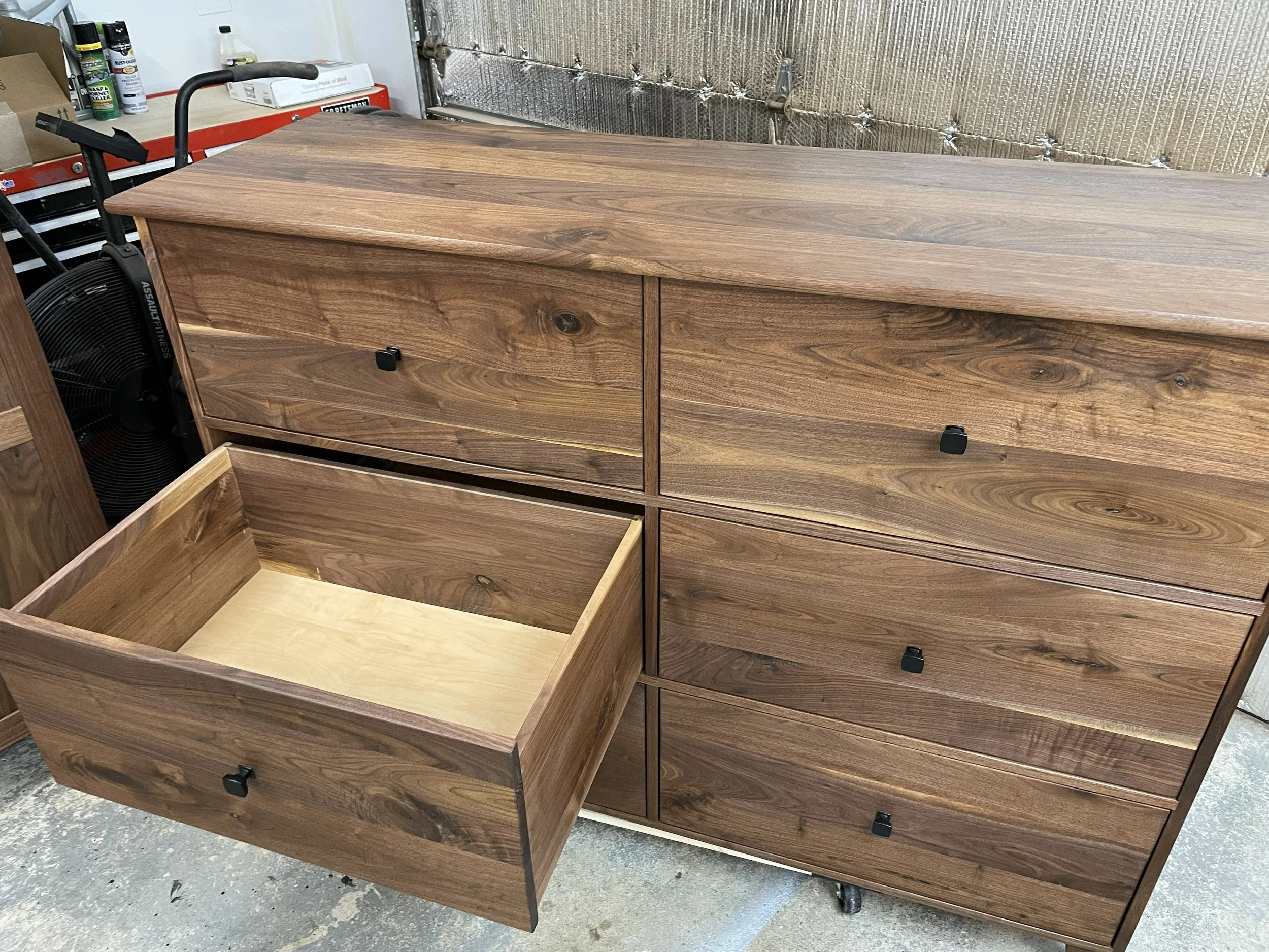 A custom walnut wooden dresser with six drawers, one of which is open, showing the interior. The dresser has a natural wood finish with visible knots and wood grain patterns.