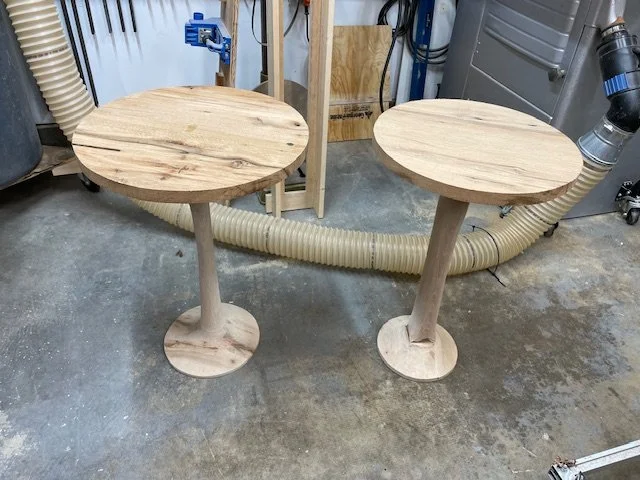 Round oak wood side tables with hand sculpted pedestal bases in the shop under construction. 