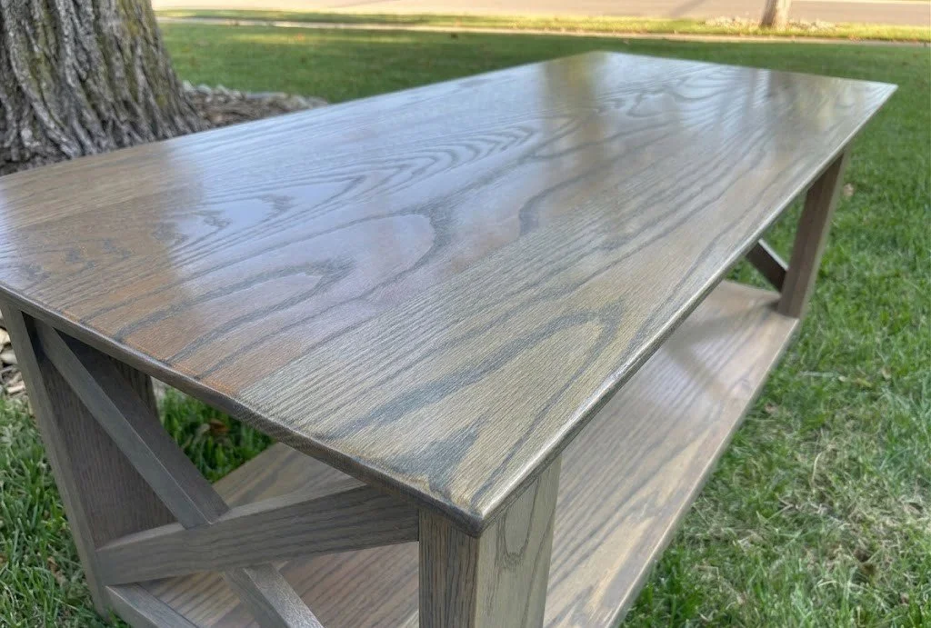 Gray red oak farmhouse style coffee table with cross ends and bottom shelf and a satin finish. 