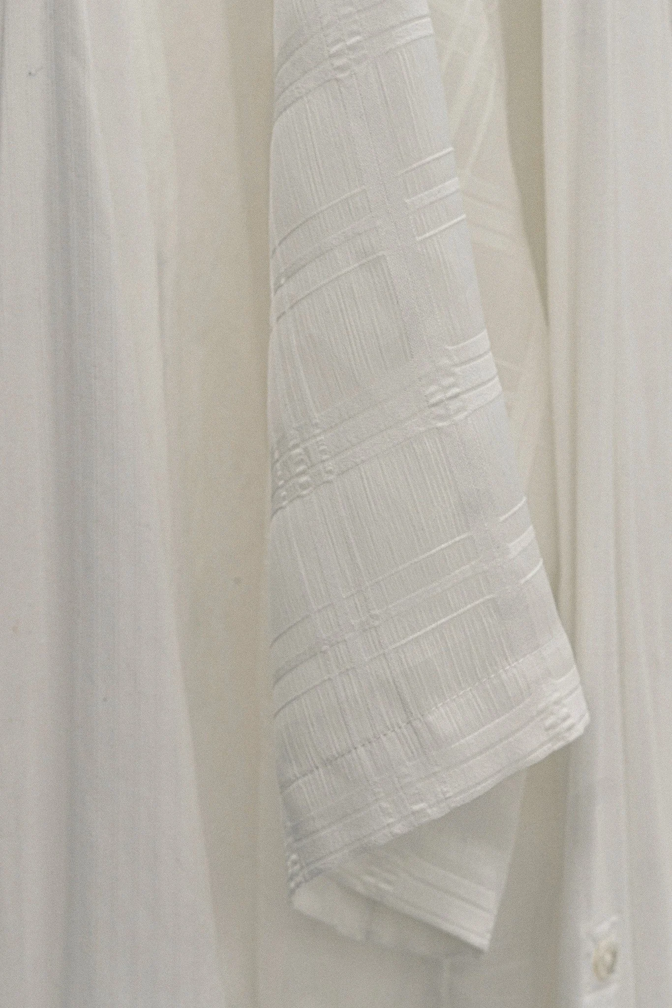 Une robe blanche en tissu léger avec un motif de rayures          horizontales, suspendue ou reçue enfaçe d'un mur ou d'une porte.