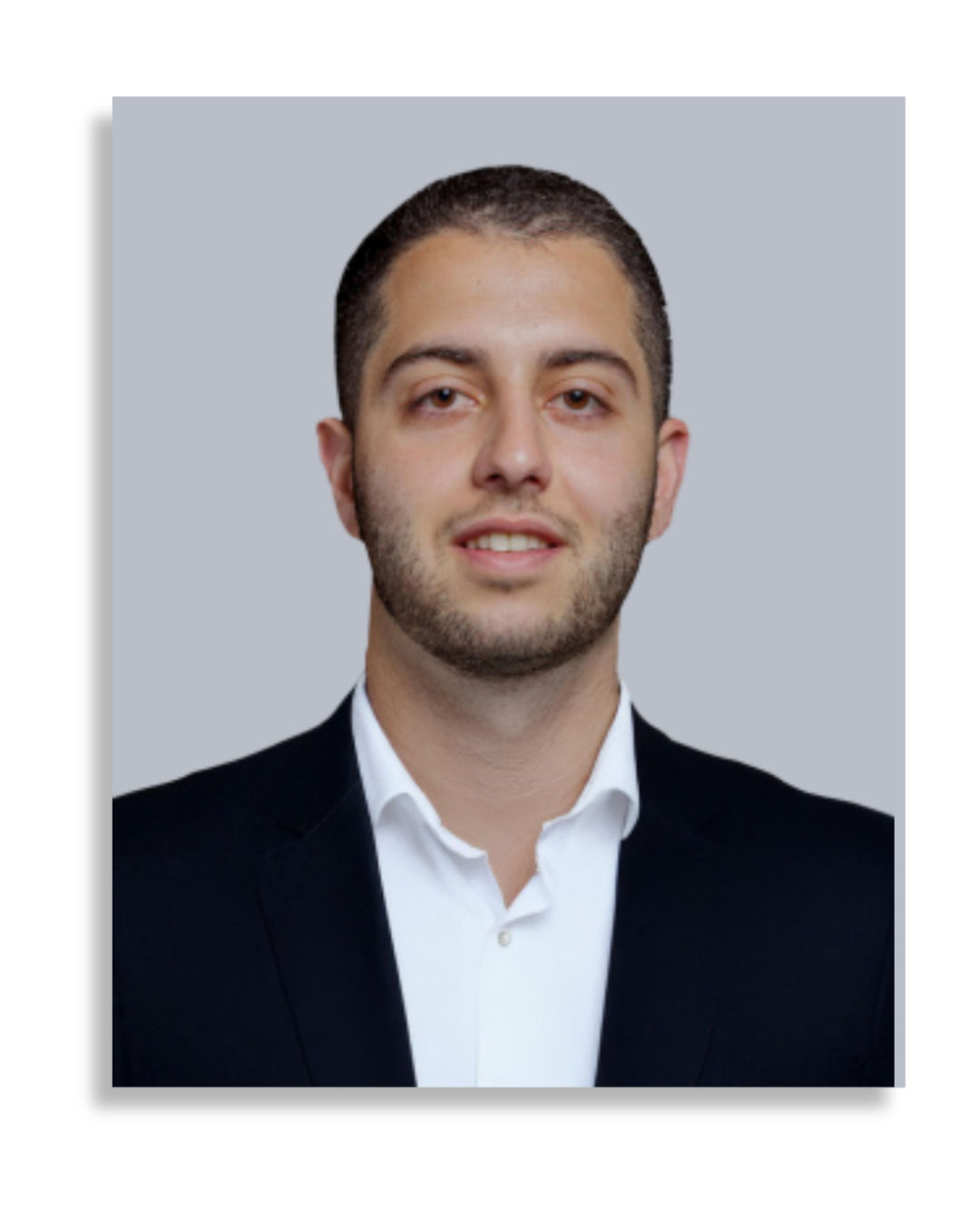 Professional headshot of a young man with short dark hair and a light beard, wearing a black suit jacket and white collared shirt, against a light gray background.