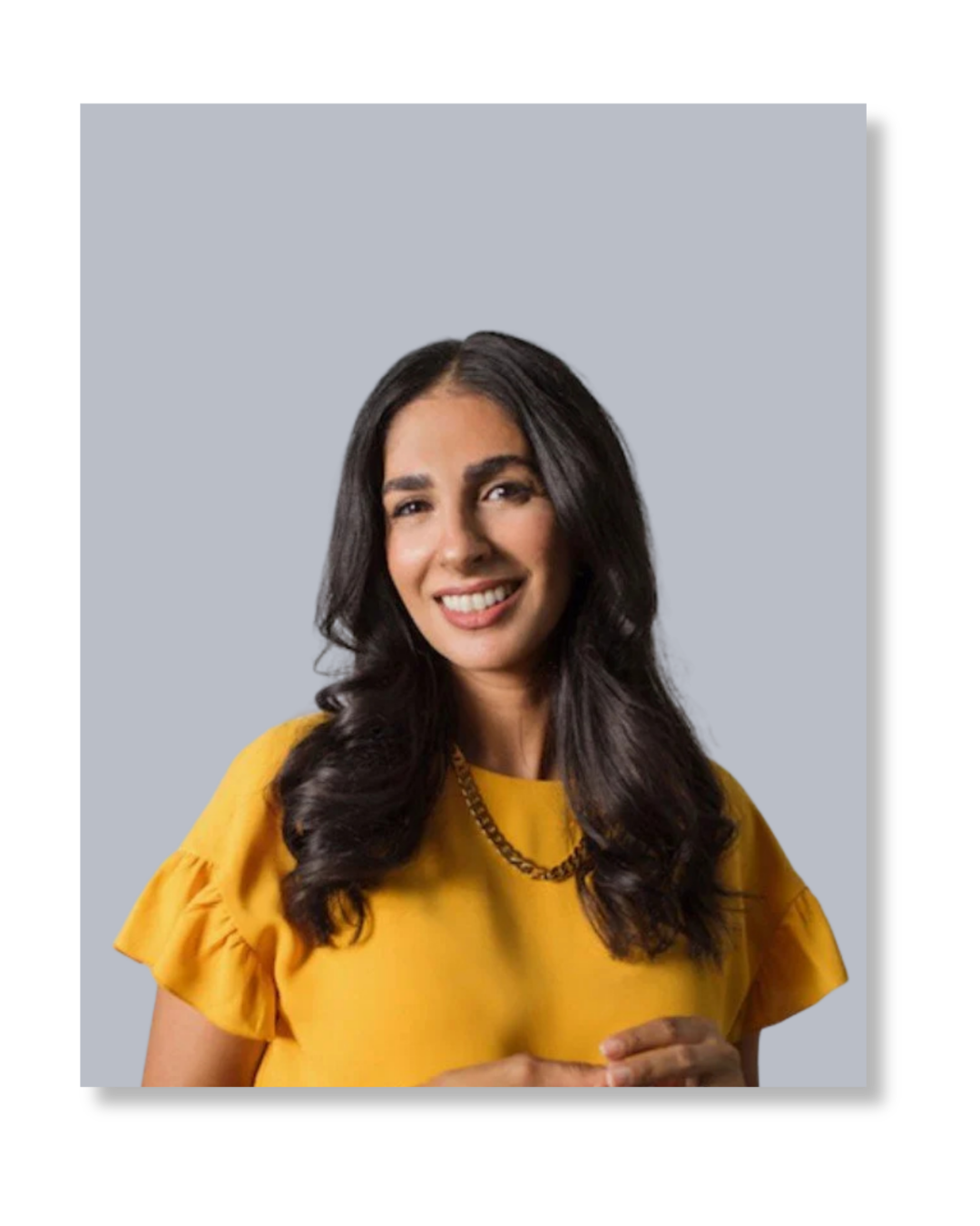 A woman with long dark hair, wearing a yellow top and a gold chain necklace, smiling against a light gray background.